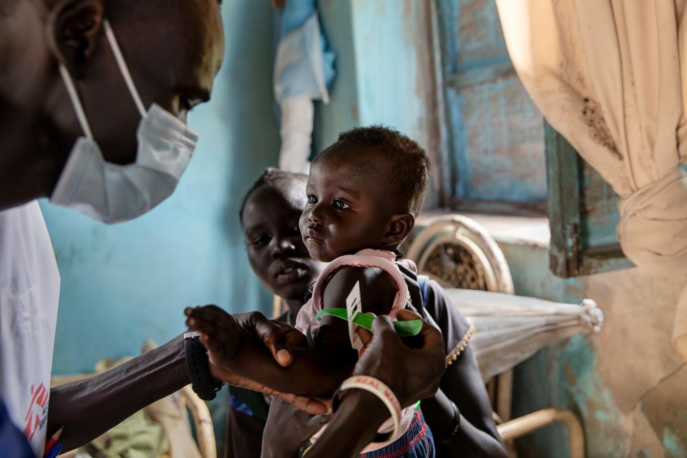 A mother holds her baby as a member of MSF staff measures the child’s level of nutrition in her house near the village of Kuom. South Sudan, 2021. © Adrienne Surprenant/Item