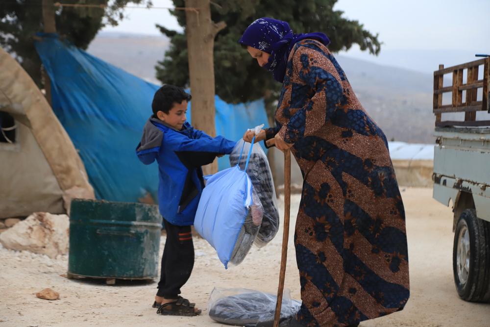 A displaced woman and a boy are holding winter kit distributed by Doctors Without Borders that includes children winter clothes and blankets. Syria, 2021. © MSF