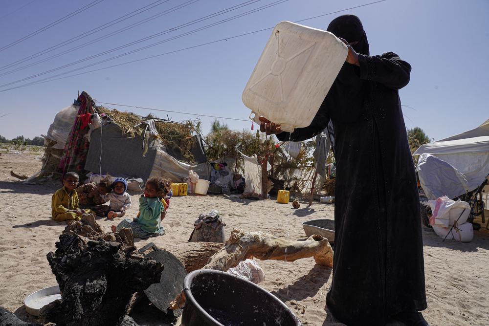 A woman pours the last drops of water from a bottle to prepare food next to her tent in the Al-Khuseif camp for internally displaced people in Marib, Yemen.