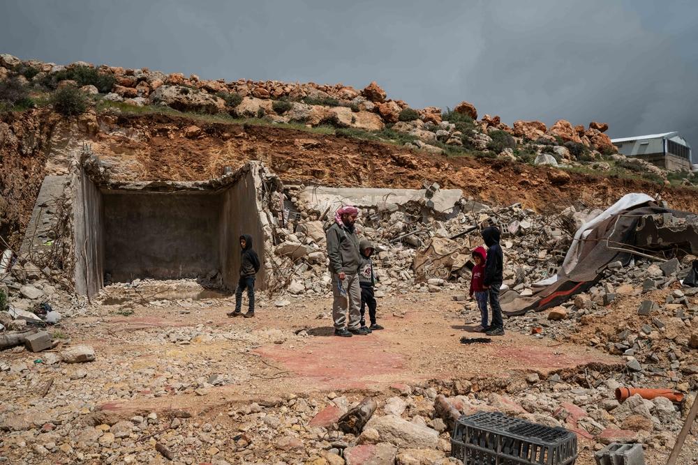 Mustafa Mlikat stands with his children next to the rubble of his house demolished by Israeli forces, in Douma. Palestine, April 2023. © Samar Hazboun