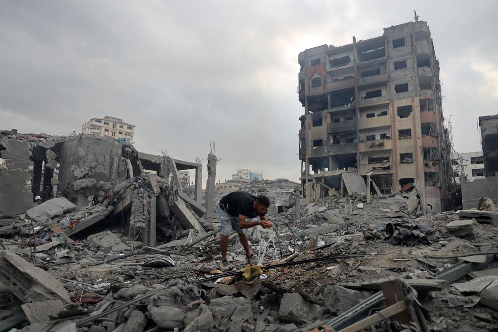 A man drinks water from a burst pipe amongst destroyed buildings in Gaza, following the outbreak of war between Israel and Hamas three days earlier. Gaza Strip, Palestine, 10 October 2023. © Mohammed Baba