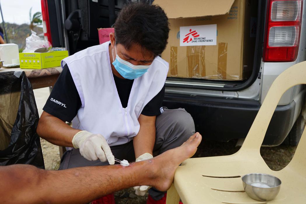 Nurse Daryll Von Abellon cleans a leg wound on a teenaged boy. Philippines, November 2024.